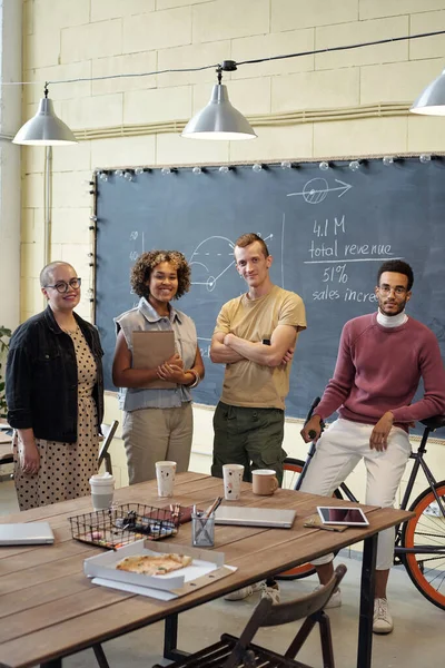 Glückliche junge Ökonomen stehen im Großraumbüro am Tisch — Stockfoto