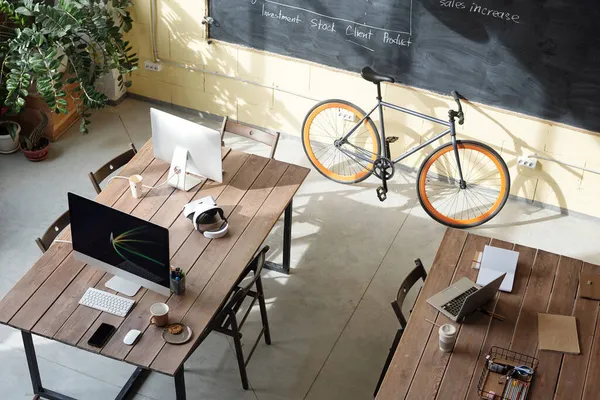 在黑板旁边有两张桌子，上面有电脑、笔记本电脑和自行车 — 图库照片