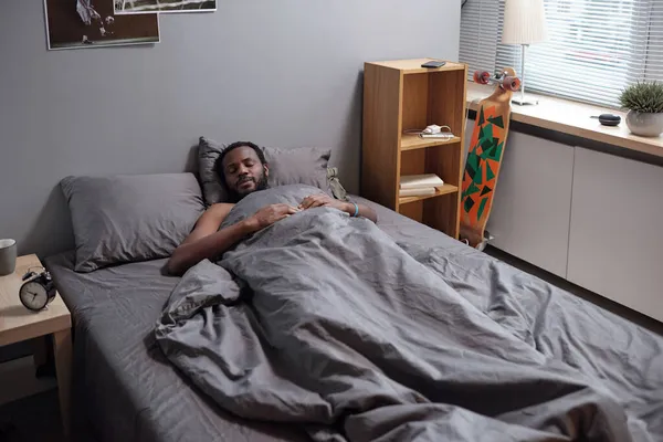 Jonge Afrikaanse man ligt onder grijze deken tijdens het slapen — Stockfoto