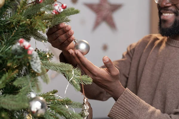 Hand van jonge Afrikaanse man met kleine zilveren speelgoed bal opknoping op xmas boom tak — Stockfoto