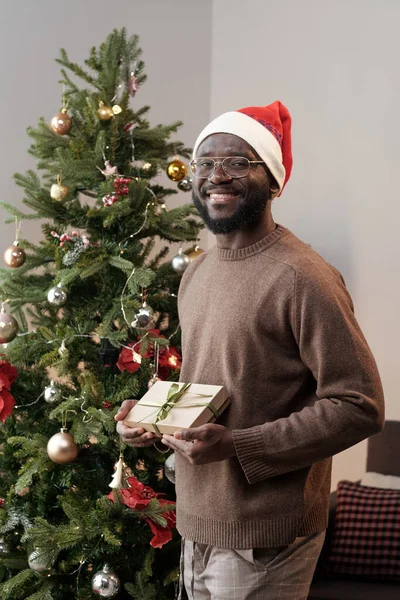 Mladý usmívající se Afričan v Santa čepici drží zabalený dárek — Stock fotografie
