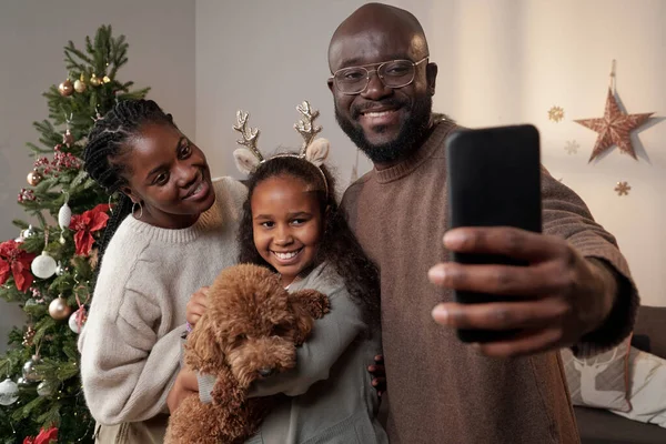 Padres felices y su linda hija con mascota haciendo selfie —  Fotos de Stock