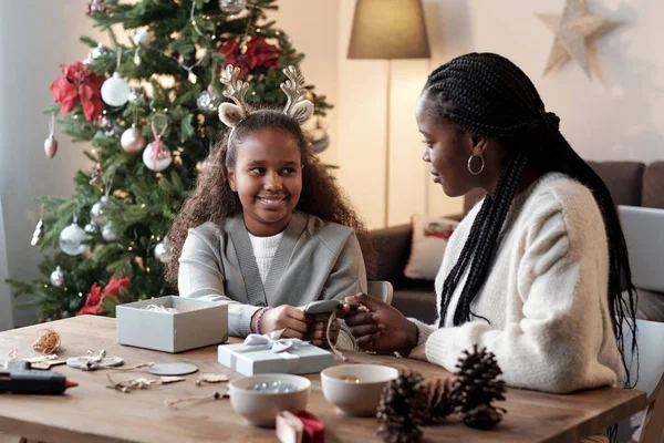 Gelukkig klein meisje en haar moeder kijken naar elkaar tijdens het inpakken van kerstcadeaus — Stockfoto