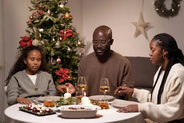 Drie familieleden van Afrikaanse etniciteit bidden door feestelijke tafel — Stockfoto