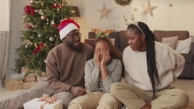 Orta boy mutlu Afrika kökenli Amerikalı anne ve baba oturma odasında oturmuş ve 10 yaşındaki kızlarına sürpriz yaparken Boks Günü hediyesiyle. Arka planda Noel ağacı