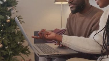 Mutlu Afro-Amerikalı kadın ve erkeğin oturma odasında Noel ağacı süslenmiş bir şekilde otururken dizüstü bilgisayar kullanırken sohbet edişlerini çek.