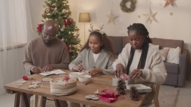 Üç kişilik Afro-Amerikan bir ailenin Noel ağacıyla oturma odasında oturması ve hediyelerini hazırlaması.