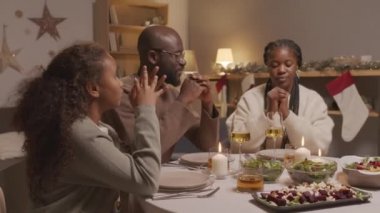 Afrika asıllı Amerikalı erkek, kadın ve 10 yaşındaki kızın Noel yemeğinden önce yemek masasında oturup dua etmelerinin el kamerası görüntüleri.
