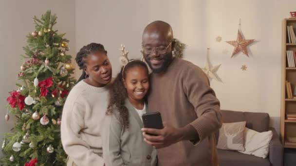 Ruční sledování šťastné afroamerické rodiny tří lidí, kteří berou selfie v obývacím pokoji s zdobeným vánočním stromečkem