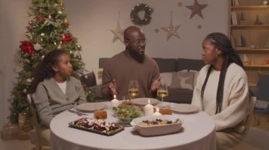 Afro-Amerikan baba, anne ve 10 yaşındaki kızının oturma odasında Noel ağacıyla oturup şükran duası ederken çekilmiş bir fotoğrafı.