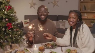 Afro-Amerikan erkek ve maytaplı bir kadının el yapımı portresi. Noel ağacında yemek masasında oturmuş kameraya gülümsüyor.