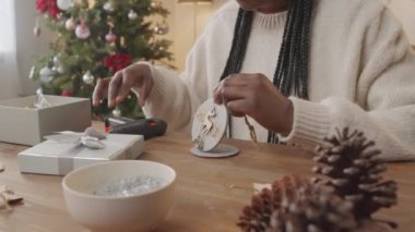 El kamerasıyla tanınmayan Afro-Amerikan bir kadının Noel ağacıyla oturma odasında oturması ve kameraya el yapımı ahşap süslemeler göstermesi.