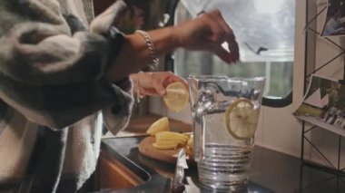 Tanınmayan genç bir kadının yazın karavanında ferahlatıcı bir içecek hazırlarken limon dilimlerini bir sürahi suya koymasının orta bölüm yavaşlığı.