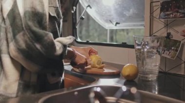 Yaz günü kamp alanında park etmiş karavanının küçük mutfağında limon dilimleyen genç bir kadının orta bölüm fotoğrafı.