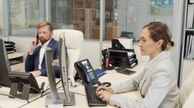 Ofiste çalışan iş adamlarının görüntüsü. İş kadını bilgisayarda yazıyor ve iş adamı telefonda konuşuyor.