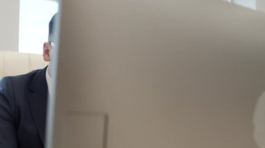 Ofiste bilgisayar üzerinde çalışan takım elbiseli ve gözlüklü ciddi bir erkek yöneticinin izini sürüyorum.