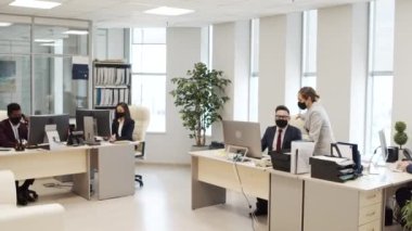 Ofisteki bilgisayarlarda çalışan takım elbiseli ve yüz maskeli iş adamlarının fotoğrafını çekiyorum. İş kadını iş adamıyla iş hakkında konuşuyor