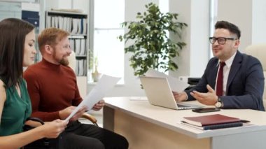 Elde çekilen, neşeli erkek finansal danışman ve müvekkilleri karşılıklı oturup ofiste sohbet ediyorlar.