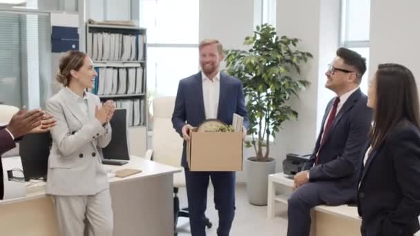 同僚が拍手と別れを言っている間 彼の所有物とオフィスを離れると段ボール箱を拾うスーツで幸せなビジネスマンの手持ち追跡ショット — ストック動画