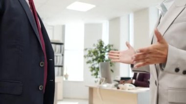 Takım elbiseli iş kadını ve tanınmayan iş adamının konuşmalarının ve ofiste tokalaşmalarının orta bölümdeki yakın çekim görüntüleri.