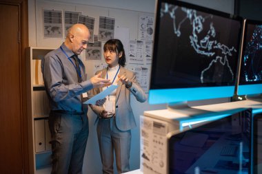 İki meslektaş iş belgeleriyle beyaz tahtada dururken kağıt tartışıyorlar.