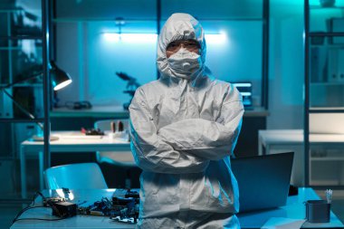 Koruyucu iş kıyafetli genç bir kadın dizüstü bilgisayar ve donanımla masanın karşısında duruyor.