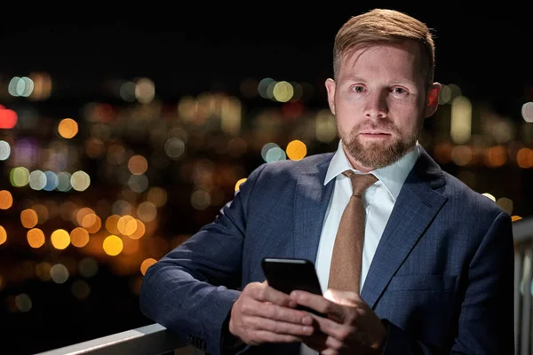 Giovane uomo d'affari serio con smartphone in piedi sul balcone di notte — Foto Stock
