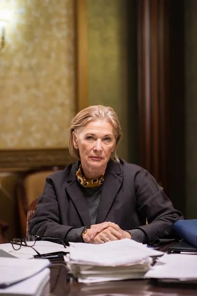 Fiducioso maturo avvocato femminile che ti guarda mentre sei seduto sul posto di lavoro — Foto Stock