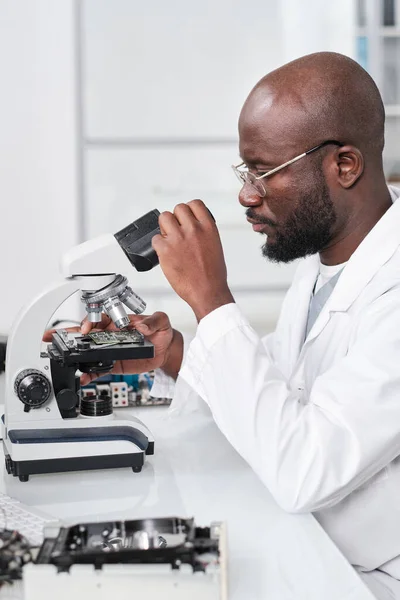 Fiatal, komoly tudós, aki mikroszkóppal néz — Stock Fotó