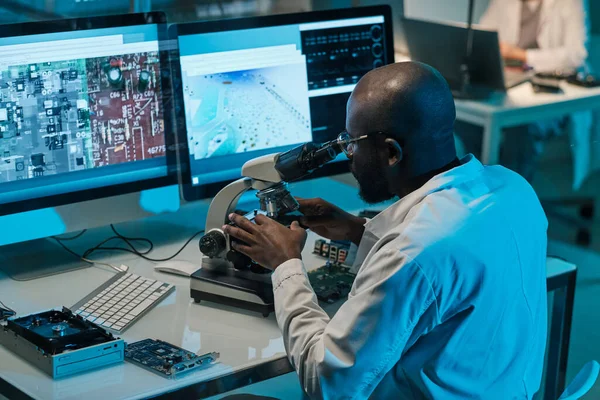 Científico africano con microscopio trabajando frente a monitores de ordenador — Foto de Stock
