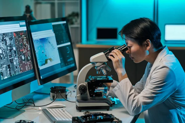 Científica asiática mirando en el microscopio durante la investigación — Foto de Stock