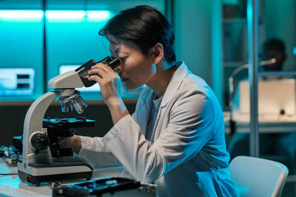 Joven trabajador serio de laboratorio mirando el microchip en el microscopio — Foto de Stock