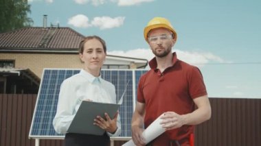 Banliyö bölgesinin dışında kameraya poz veren dosya ve erkek mühendis kadın yöneticisinin portresinin takibi. Arka plandaki güneş panelleri