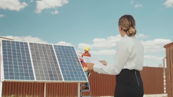 郊外に太陽光パネルを設置する男性技術者への指示書付き女性監督者の追跡 — ストック動画