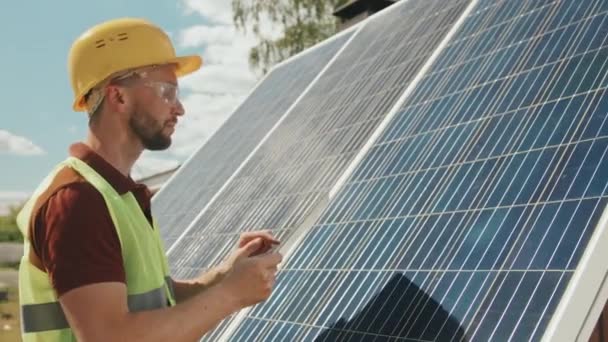 安全ゴーグル ベスト ハード帽子の男性エンジニアの追跡ショットタブレットを使用して太陽電池パネルを外でチェック — ストック動画