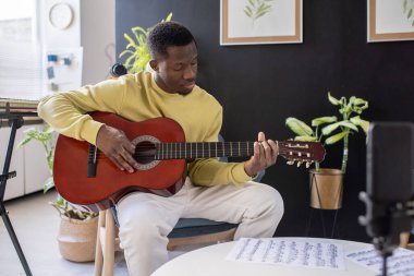Akıllı telefon kamerasının önünde gitar çalan ciddi bir Afrikalı.