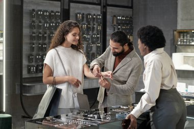 Genç adam mücevher mağazasında güzel bir kadının bilekliğine bilezik takıyor.