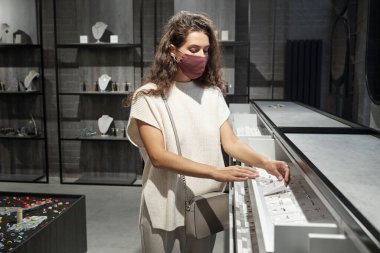 Koruyucu maskeli genç bayan yeni yüzük seçiyor.