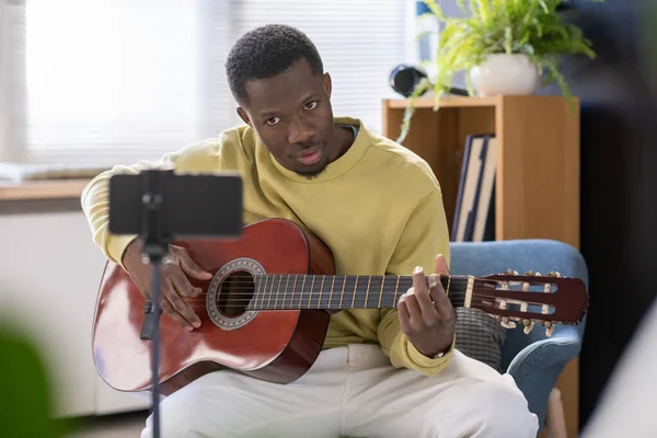 Genç müzik öğretmeni gitar çalıyor ve akıllı telefon kamerasına bakıyor. — Stok fotoğraf