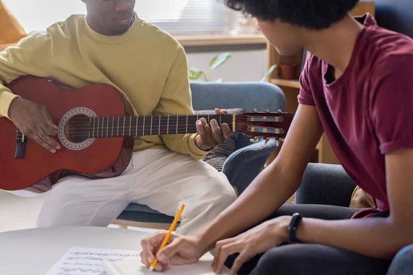 Молодой парень делает заметки и смотрит на учителя музыки, играющего на гитаре — стоковое фото