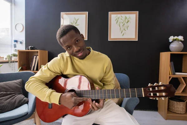 Akustik gitarlı, kameranın önünde oturan gülümseyen Afrikalı genç adam. — Stok fotoğraf