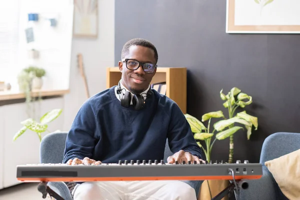 Vrolijke jongeman in bril en casualwear zittend op piano toetsenbord — Stockfoto