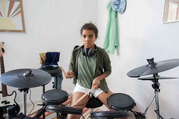 Serious schoolgirl in casualwear beating drums with drumsticks — Stock Photo, Image