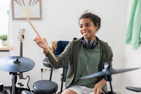 Joyeux écolière mignonne avec pilons frappant tambours à la leçon de musique — Photo