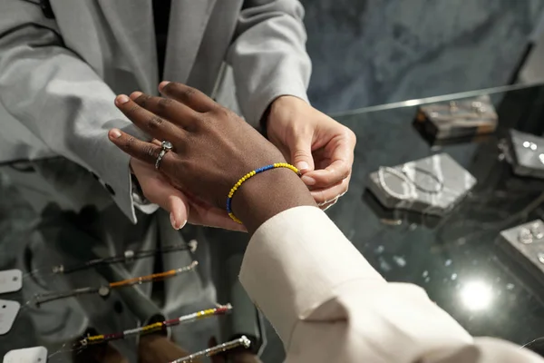 Asistente de joyería femenina poniendo pulsera en la mano de la mujer joven — Foto de Stock