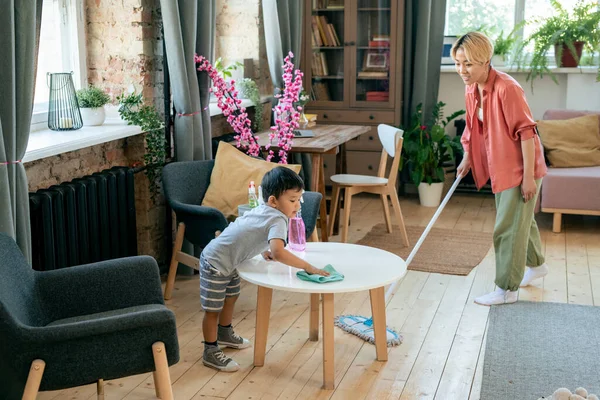 Fiatal nő takarítás padló, míg a fia törlése asztal fertőtlenítő — Stock Fotó