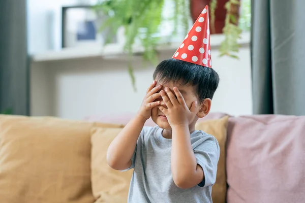 Aranyos kisfiú szülinapi sapkában, eltakarja a szemét. — Stock Fotó