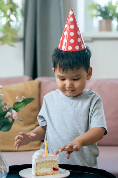 Schattig jongetje in verjaardagsmuts aanraken stukje taart met kaars — Stockfoto