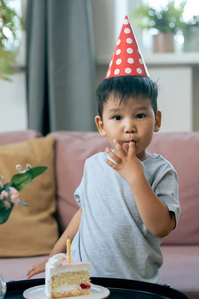 Чарівний маленький хлопчик в шапці для дня народження дегустаційний торт і дивиться на камеру — стокове фото