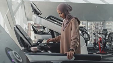 Koşu bandındaki tesettürlü Müslüman kadın spor salonunda antrenman yaparken koşmaya başlıyor.